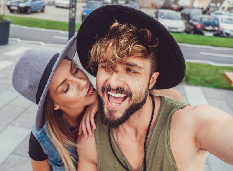 Freundin, die Freund küsst, während er selfie nimmt lizenzfreies stockfoto Freundin, die Freund küsst, während er selfie nimmt lizenzfreies stockfoto