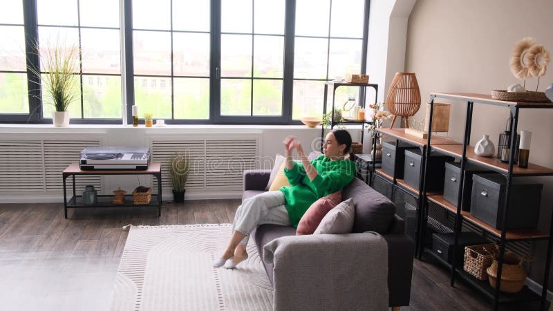 Freundliche Frau, die sich auf dem Sofa entspannt und sich zu Hause oder in der Wohnung ausstreckt stock footage