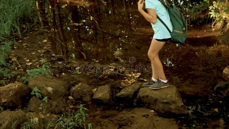 Fria turister flickor korsar floden. som vandrar i skogen med ryggsäck. En ung flickvän går över floden på