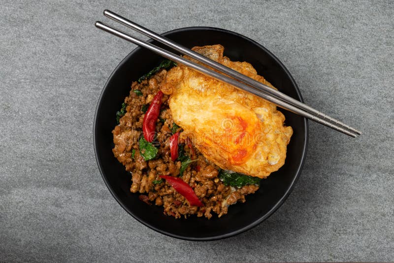 Fried Basil Pork with Fried Egg and White Rice in Black Bowl on the