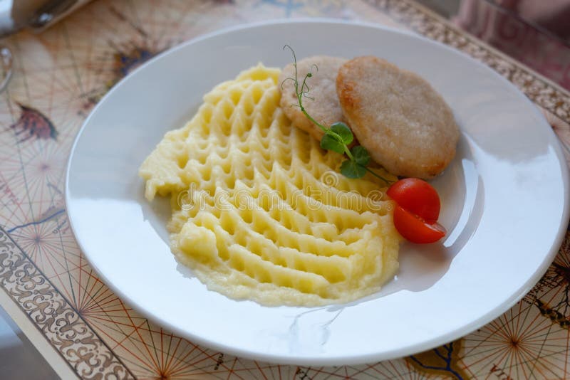 Fried cutlet with mashed potatoes and red fresh tomato on the white plate on the table. Serving of restaurant