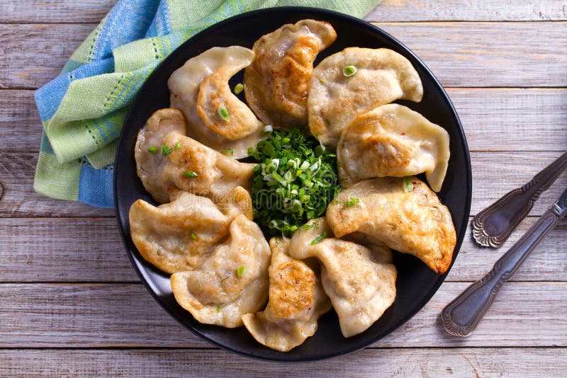 Fried dumplings stuffed with meat and served with chopped parsley and spring onion on a black plate on a wooden rustic table.