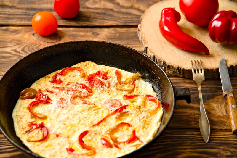 Fried eggs in a cast iron pan with red tomatoes and peppers. wooden table. stock images