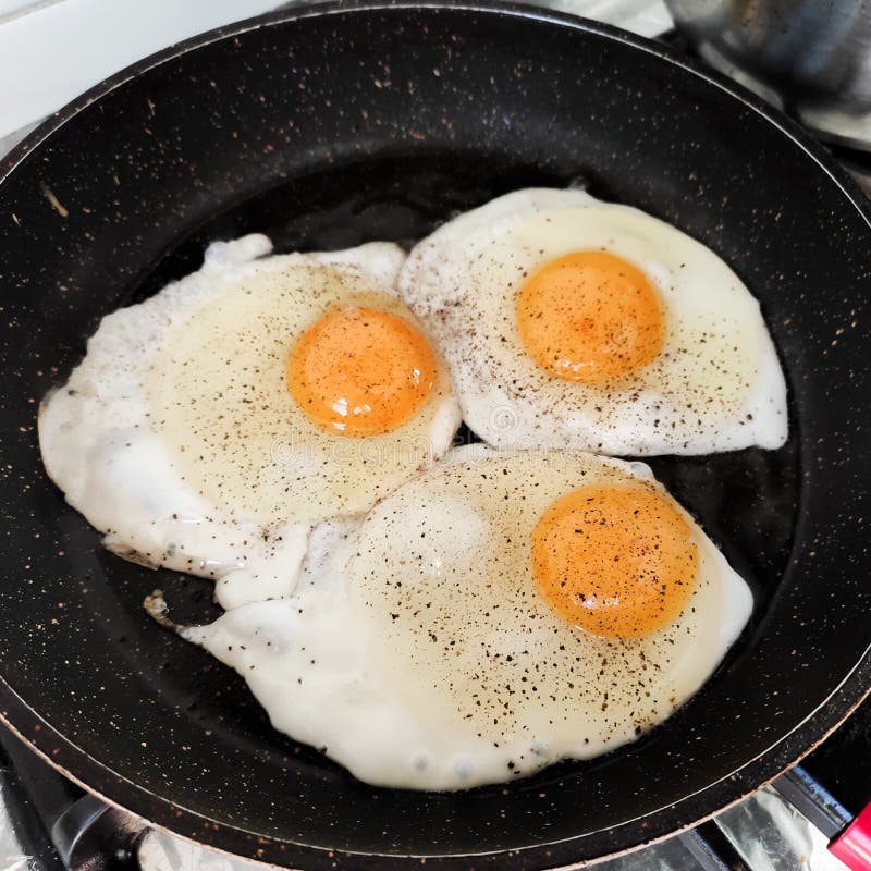 Fried Eggs Close Up. Eggs Fried in a Black Pan. Three Egg Breakfast