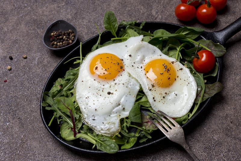 Fried eggs sunny side up on pan with herbs, cherry tomatoes and pepper, with fork an brown background. Concept of healthy stock photos Fried eggs sunny side up on pan with herbs, cherry tomatoes and pepper, with fork an brown background. Concept of healthy stock photos