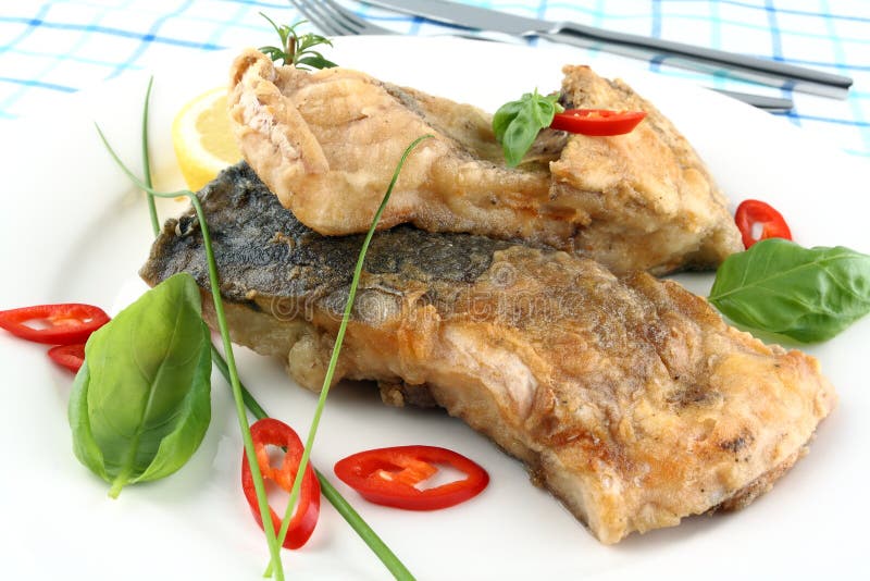 Fried fish on white plate, fork and knife