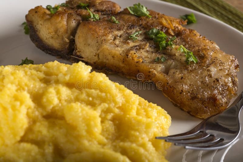 Fried Fish Woth Polenta and Herbs on Plate with Fork Stock Photo