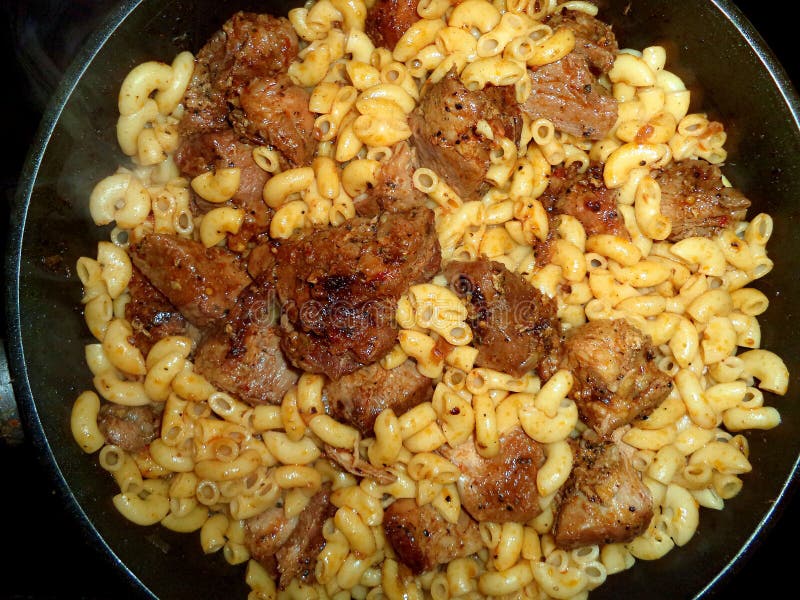 Pieces of meat with pasta in a frying pan royalty free stock photo