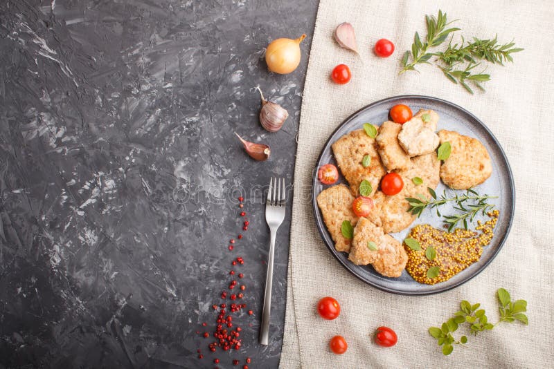 Fried pork chops with tomatoes and herbs on a gray ceramic plate on a black concrete background.  top view, copy space