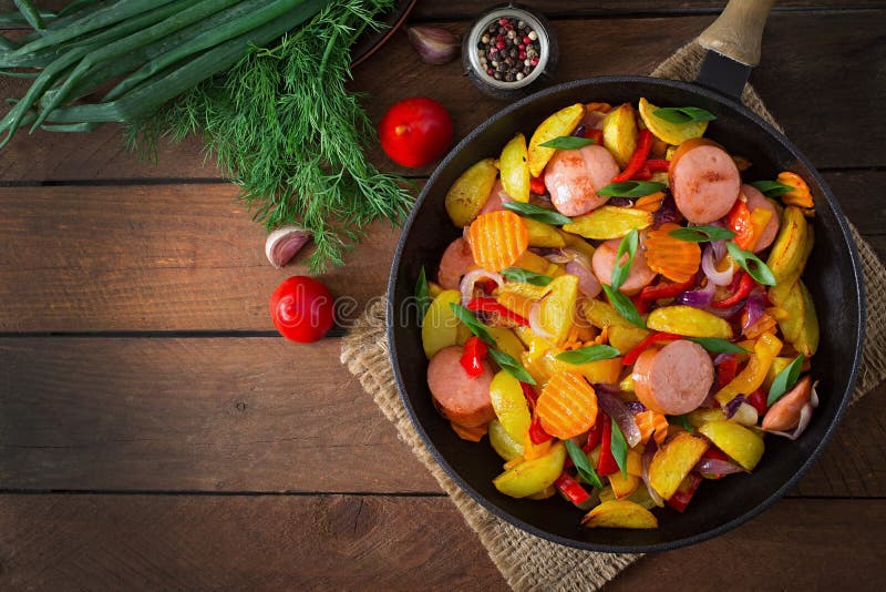 Fried potatoes with vegetables and sausages. Top view