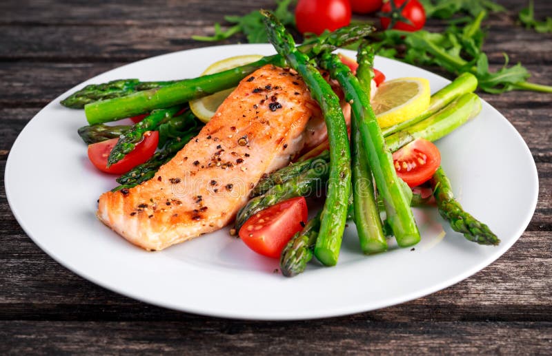 Fried salmon with asparagus, tomatoes, lemon, yellow lime on white plate