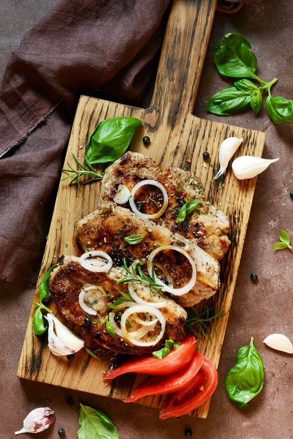 Fried steak with herbs and spices on wooden board with tomato, garlic, onion rings, rosemary and fresh basil royalty free stock images Fried steak with herbs and spices on wooden board with tomato, garlic, onion rings, rosemary and fresh basil royalty free stock images