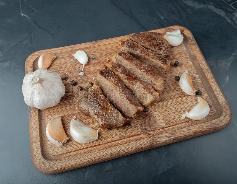 Fried steak pieces on a wooden board and garlics stock illustration