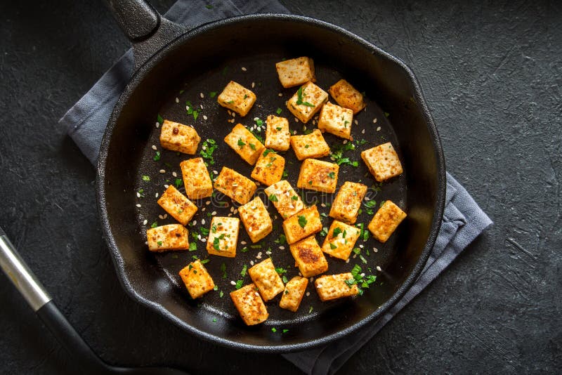 Fried tofu. With sesame seeds and spices on cast iron pan, copy space. Healthy ingredient for cooking vegan vegetarian diet food. Roasted tofu over black stock photos
