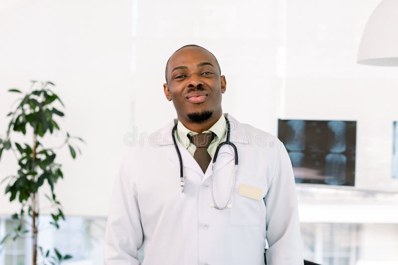 Friendly african american doctor in modern office. Male African surgeon doctor in white coat, with stethoscope royalty free stock image Friendly african american doctor in modern office. Male African surgeon doctor in white coat, with stethoscope royalty free stock image