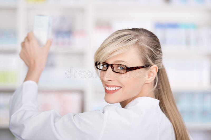 Friendly and smiling female pharmacist stores the medicines in the pharmacy shelves. Friendly and smiling female pharmacist stores the medicines in the pharmacy shelves