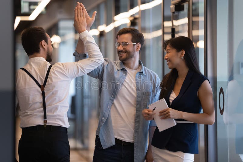 Friendly male colleagues giving high five talking in office hall