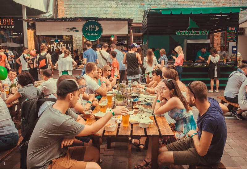 Friendly party with crowd of eating people at table during outdoor Street Food Festival