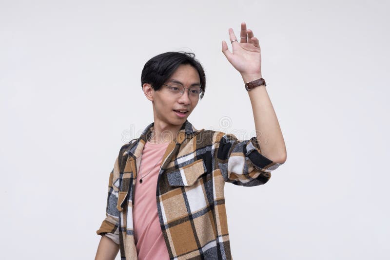 A friendly young asian man saying hello to a friend or acquaintance, waving his hand. on a white backdrop stock photo
