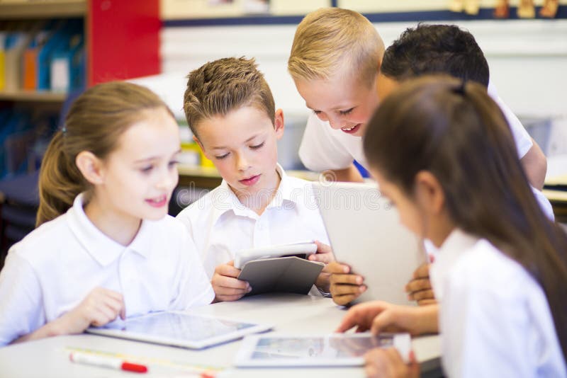 Happy students in classroom using a digital tablet, they are all wearing uniforms. Happy students in classroom using a digital tablet, they are all wearing uniforms.