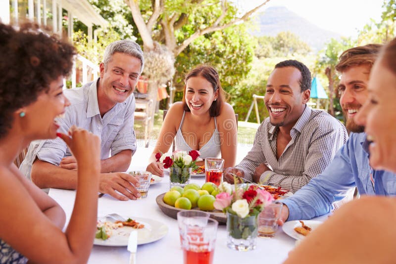 Friends dining together at a table in a garden. Domestic, group.