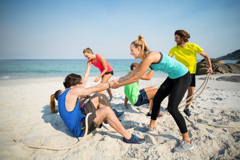 Friends helping man and woman while playing tug of war at beach
