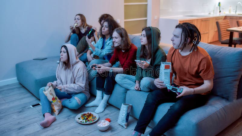 Excited multiethnic teen friends enjoying video games, free time at home, Stock image