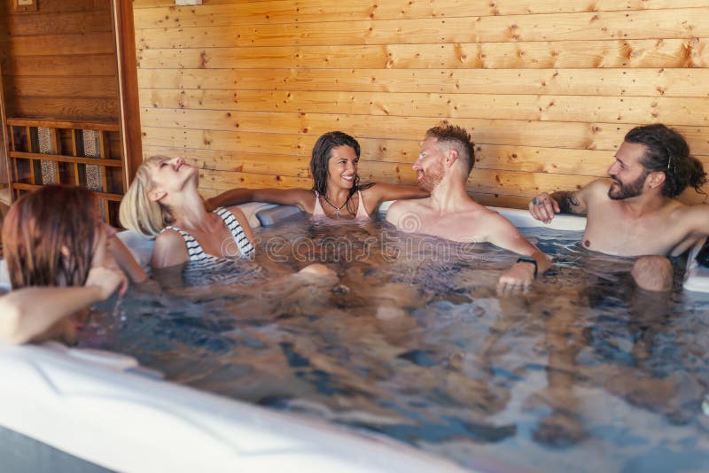 Friends relaxing in a hot tub while on a vacation. Group of cheerful young friends relaxing in a hotel resort spa center hot tub, having fun while on a vacation stock photo