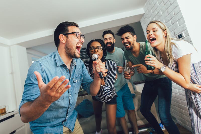 Happy friends singing together at home. Karaoke party concept