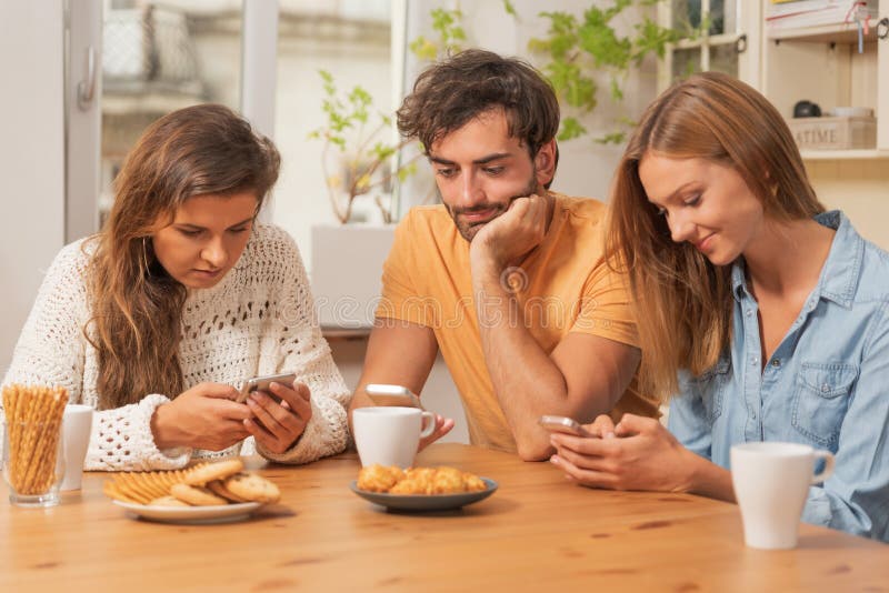 Friends sitting in the kitchen and watching on their phones stock images