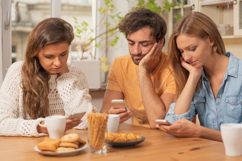 Friends sitting in the kitchen and watching on their phones stock image