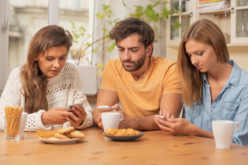 Friends sitting in the kitchen and watching on their phones royalty free stock images