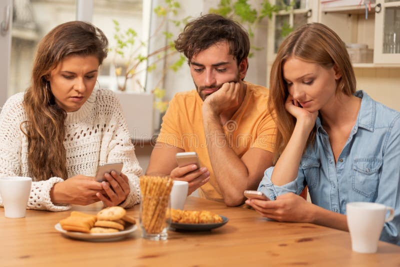 Friends sitting in the kitchen and watching on their phones royalty free stock images