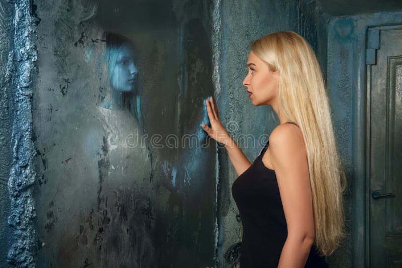 Frightened young woman looking to the mirror and seeing in reflection a ghost girl. Frightened young women looking to frozen  mirror and seeing in reflection a