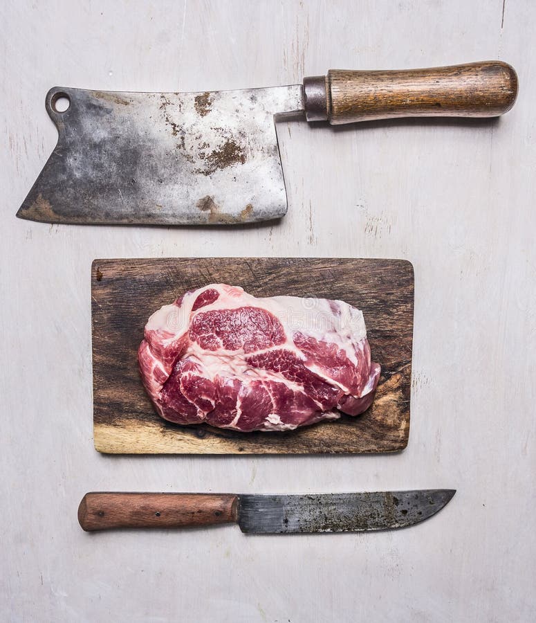 Friptură proaspătă delicioasă de porc pe o placă de tranșare cu un satâr de carne și cu un cuțit din lemn rustic, în prim-plan royalty free stock photos