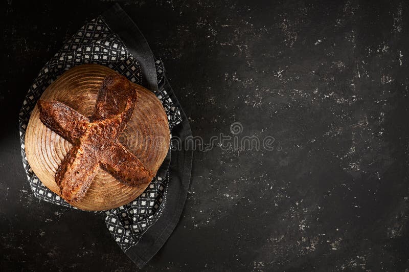 Frisch gebackenes Artisan Sourdough Brotlaibe mit Küchentuch auf schwarzem Beton Hintergrund. Frisch gebackenes Brotsalat aus Kunsthandwerk mit Küchentüchern auf schwarzem Beton Topansicht mit Kopierraum