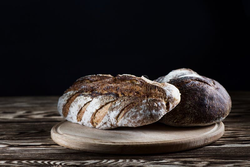 Frisch gebackenes selbst gemachtes Brot liegt auf einer runden hölzernen Platte auf einem schwarzen Hintergrund stockfoto