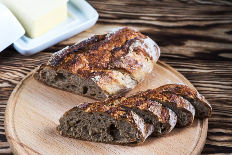 Frisch gebackenes selbst gemachtes Brot liegt auf einer runden hölzernen Platte auf einem schwarzen Hintergrund stockfotos