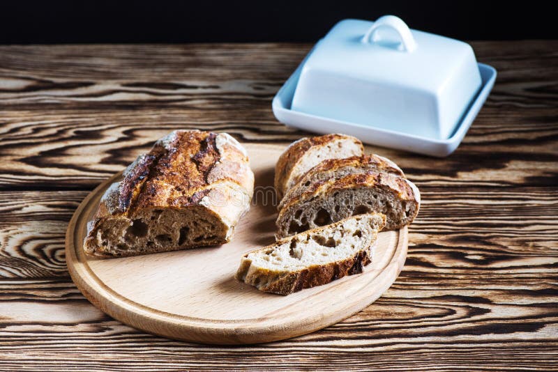 Frisch gebackenes selbst gemachtes Brot liegt auf einer runden hölzernen Platte auf einem schwarzen Hintergrund lizenzfreie stockfotos