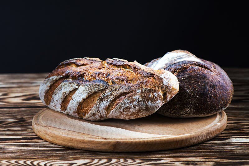 Frisch gebackenes selbst gemachtes Brot liegt auf einer runden hölzernen Platte auf einem schwarzen Hintergrund stockfotografie