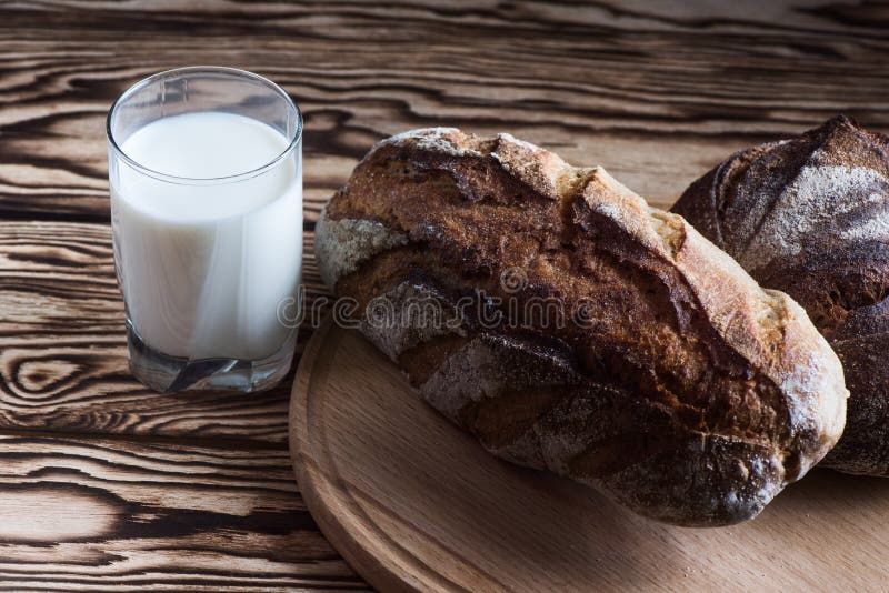 Frisch gebackenes selbst gemachtes Brot liegt auf einer runden hölzernen Platte nahe bei einem Glas Milch auf einem schwarzen Hin stockbild