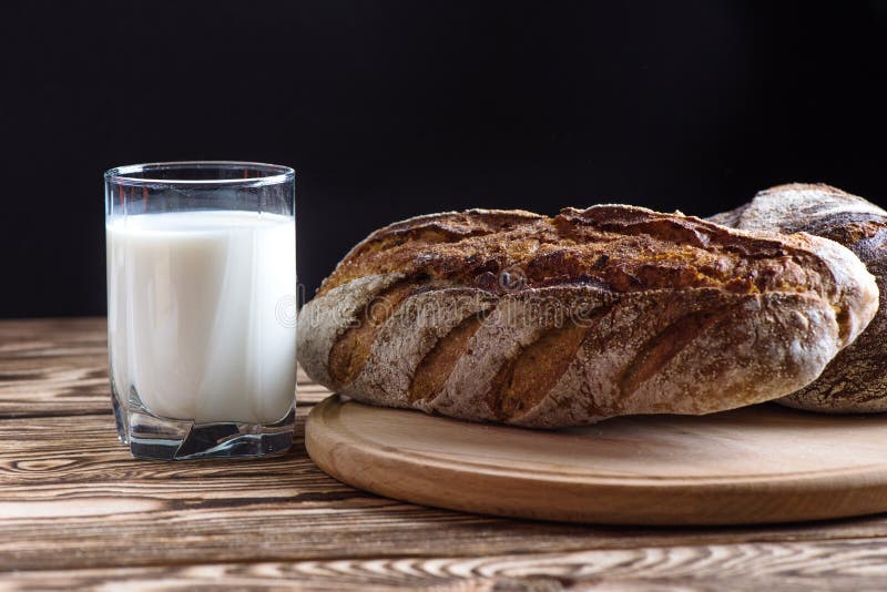 Frisch gebackenes selbst gemachtes Brot liegt auf einer runden hölzernen Platte nahe bei einem Glas Milch auf einem schwarzen Hin stockbilder