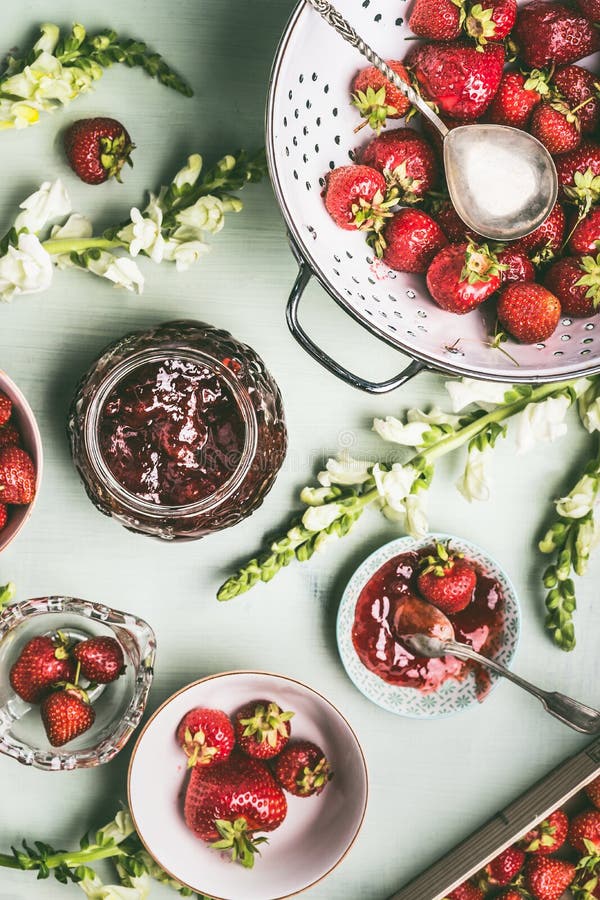 Frische Erdbeeren im Sieb und in den Schüsseln mit Stauglas und -löffel auf Küchentischhintergrund mit Gartenblumen, Draufsicht S lizenzfreie stockbilder Frische Erdbeeren im Sieb und in den Schüsseln mit Stauglas und -löffel auf Küchentischhintergrund mit Gartenblumen, Draufsicht S lizenzfreie stockbilder