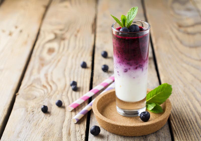 Frische gesunde Blaubeerensmoothies in einem Glas mit Beeren und tadellosen Blättern auf einem hölzernen Stand lizenzfreies stockfoto Frische gesunde Blaubeerensmoothies in einem Glas mit Beeren und tadellosen Blättern auf einem hölzernen Stand lizenzfreies stockfoto