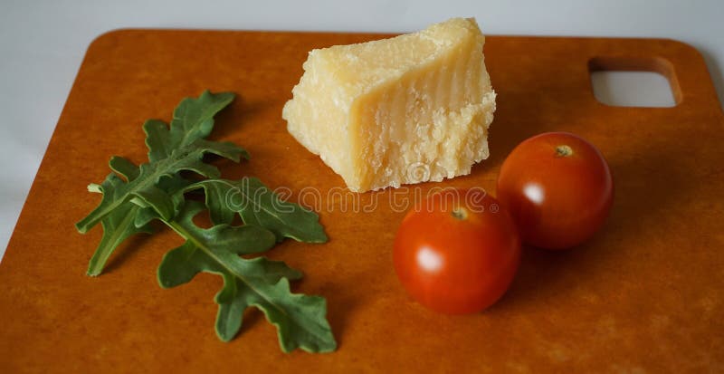 Frische grüne Arugulablätter, Kirschtomaten und Parmesankäseparmesankäse auf Hartfaserplatte stockfotografie Frische grüne Arugulablätter, Kirschtomaten und Parmesankäseparmesankäse auf Hartfaserplatte stockfotografie