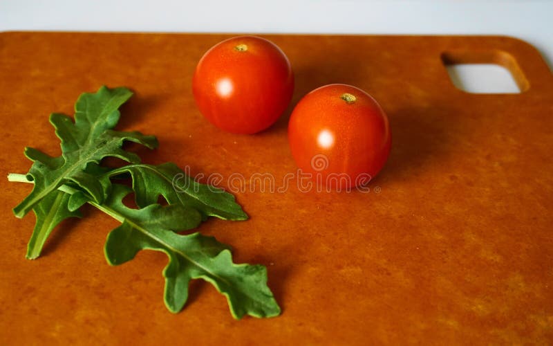 Frische grüne Arugulablätter und Kirschtomaten auf Hartfaserplatte lizenzfreie stockfotografie Frische grüne Arugulablätter und Kirschtomaten auf Hartfaserplatte lizenzfreie stockfotografie