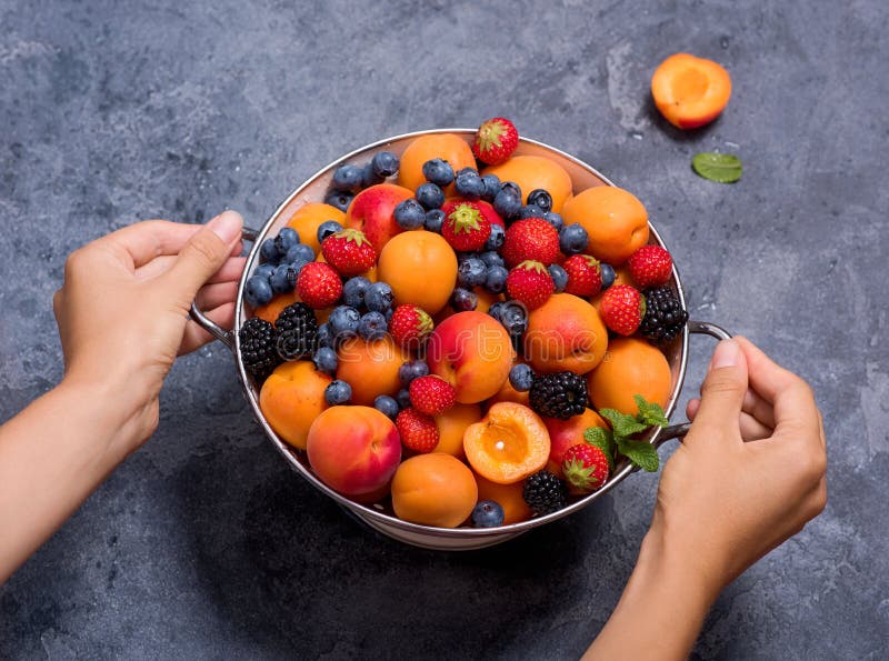 Frische Sommerfrüchte und Beeren, Aprikosen, Blaubeeren, Erdbeeren im Sieb, die Hände der Frau, die Sieb mit Früchten halten und
