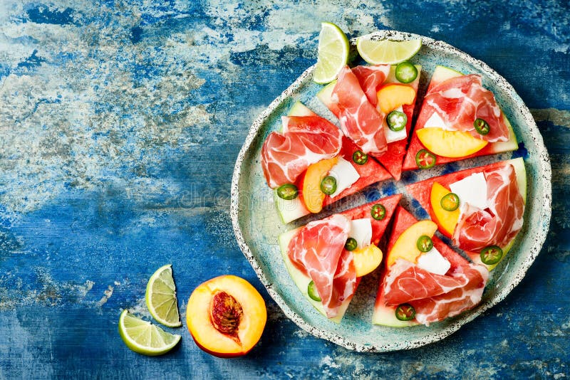 Frische Sommerwassermelonenpizza mit Feta, Pfirsich, Prosciutto, Jalapeno und Honig nieselt auf blauem Hintergrund lizenzfreie stockbilder Frische Sommerwassermelonenpizza mit Feta, Pfirsich, Prosciutto, Jalapeno und Honig nieselt auf blauem Hintergrund lizenzfreie stockbilder