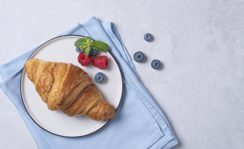 Frisches Croissant auf weißem Teller und blaue Serviette mit Beeren auf blauem Hintergrund stockbilder Frisches Croissant auf weißem Teller und blaue Serviette mit Beeren auf blauem Hintergrund stockbilder