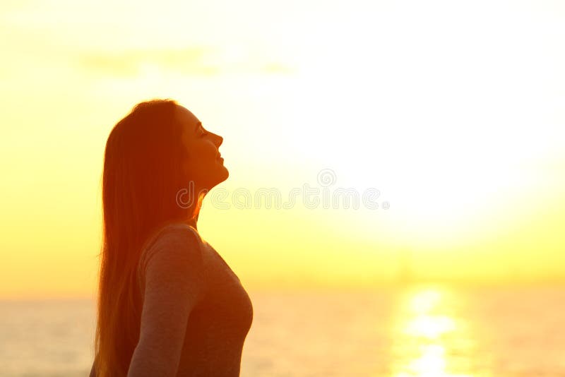 Side view portrait of a relaxed woman breathing deeply fresh air at sunset on the beach. Side view portrait of a relaxed woman breathing deeply fresh air at sunset on the beach